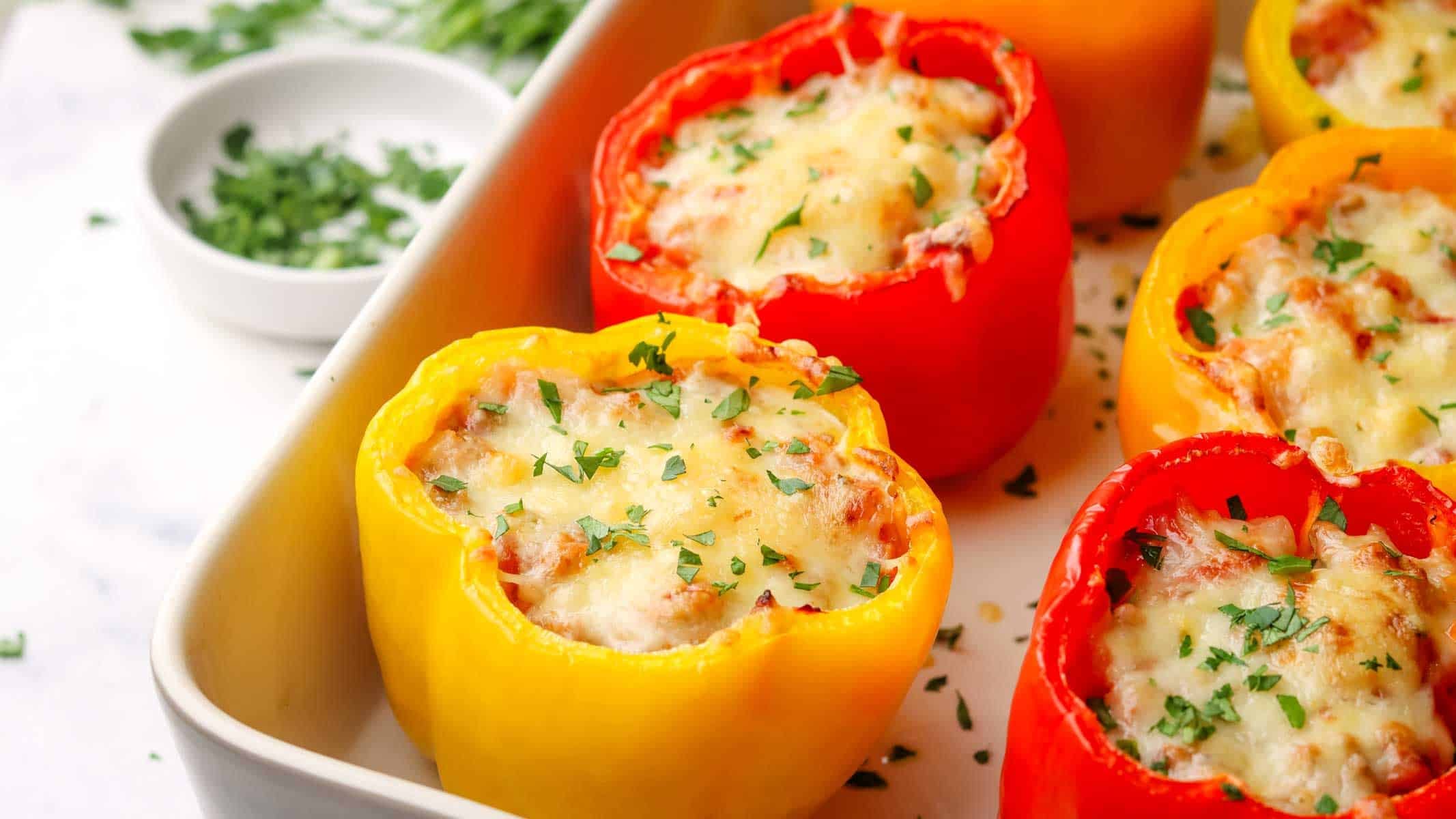 a dish with baked yellow and red peppers stuffed with turkey and rice filling and topped with cheese.