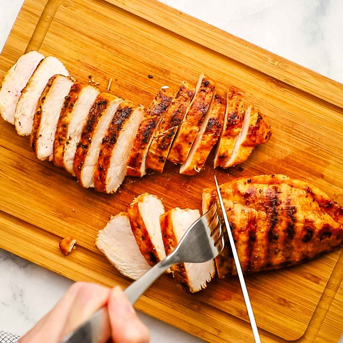 cutting chicken breasts on a wooden cutting board