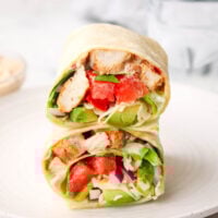 a grilled chicken wrap cut in half and stacked on top of each other on a plate.