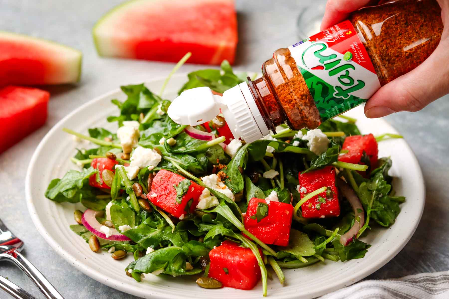 sprinkling tajin on a plate of mexican watermelon salad