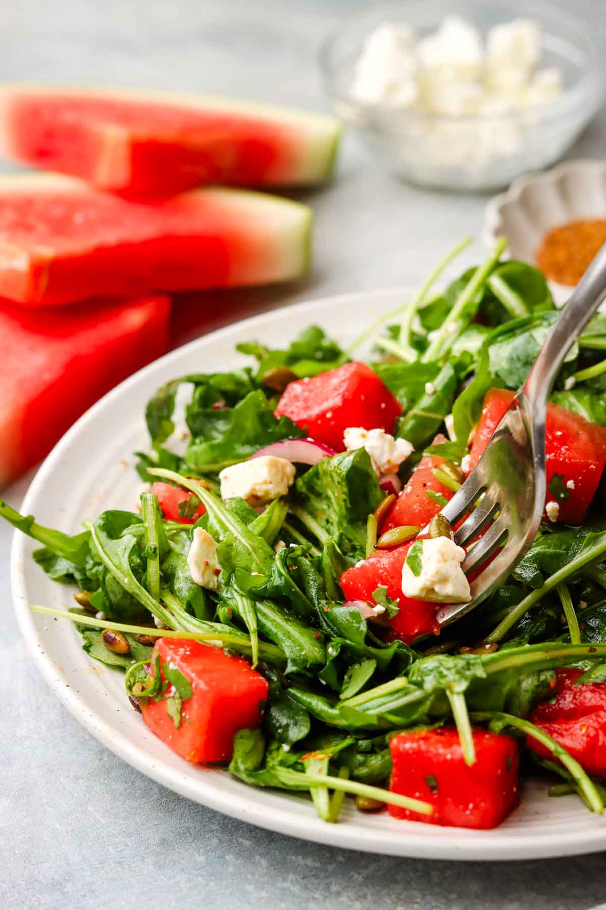 a plate of Mexican watermelon salad with watermelon slices shown in the background.