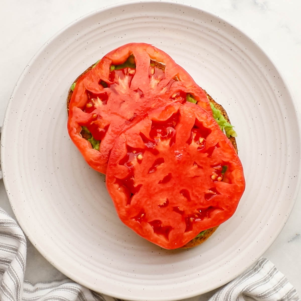 tomato slices layered on avocado mixture on toast