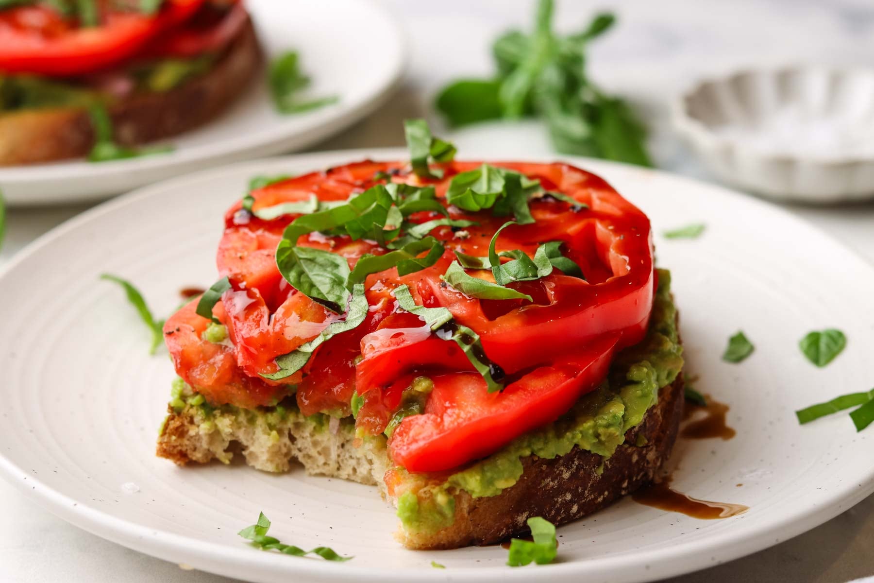 a slice of tomato avocado toast on a plate with a bite taken out of it