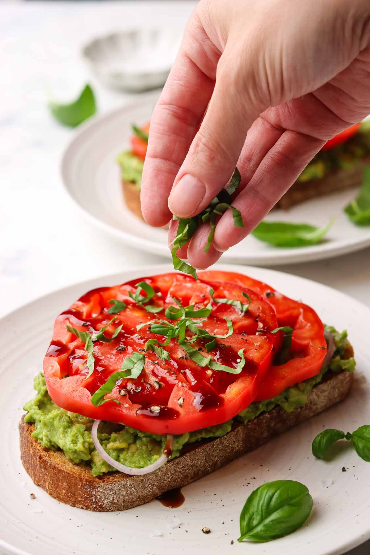 a hand sprinkling chopped fresh basil on toast