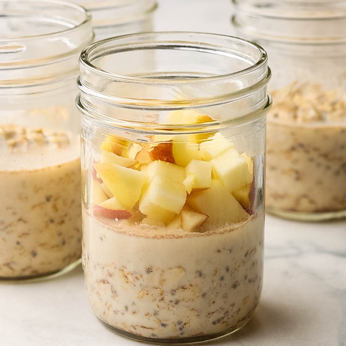 mason jars filled halfway through with oats mixture with chopped apples added on top