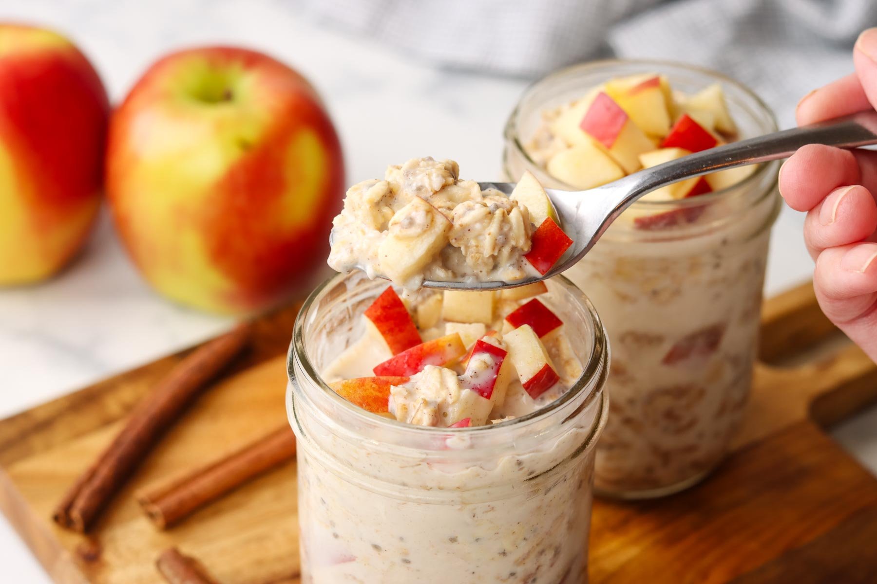 a hand picking up a spoonful of oats from a mason jar