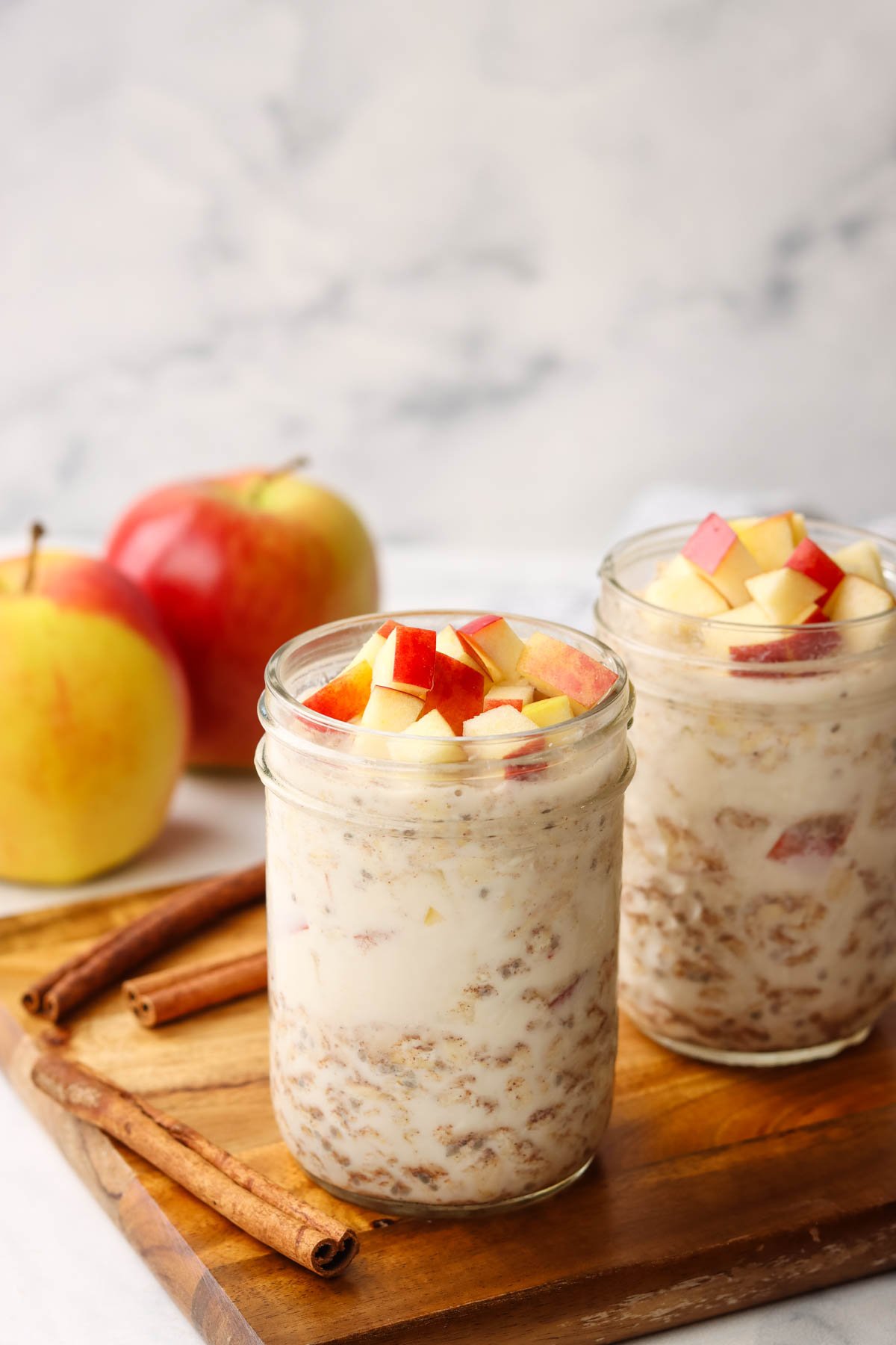 two apple cinnamon overnight oat jars on a cutting board with apples in the background