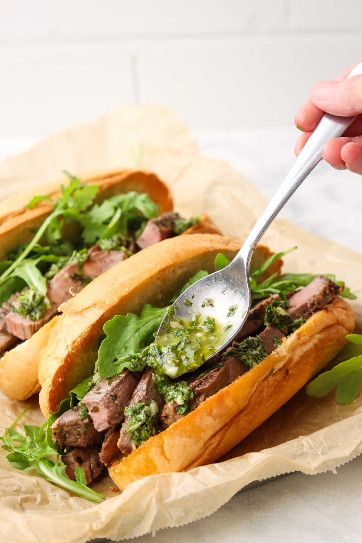 spooning chimichurri on the steak in the sandwich