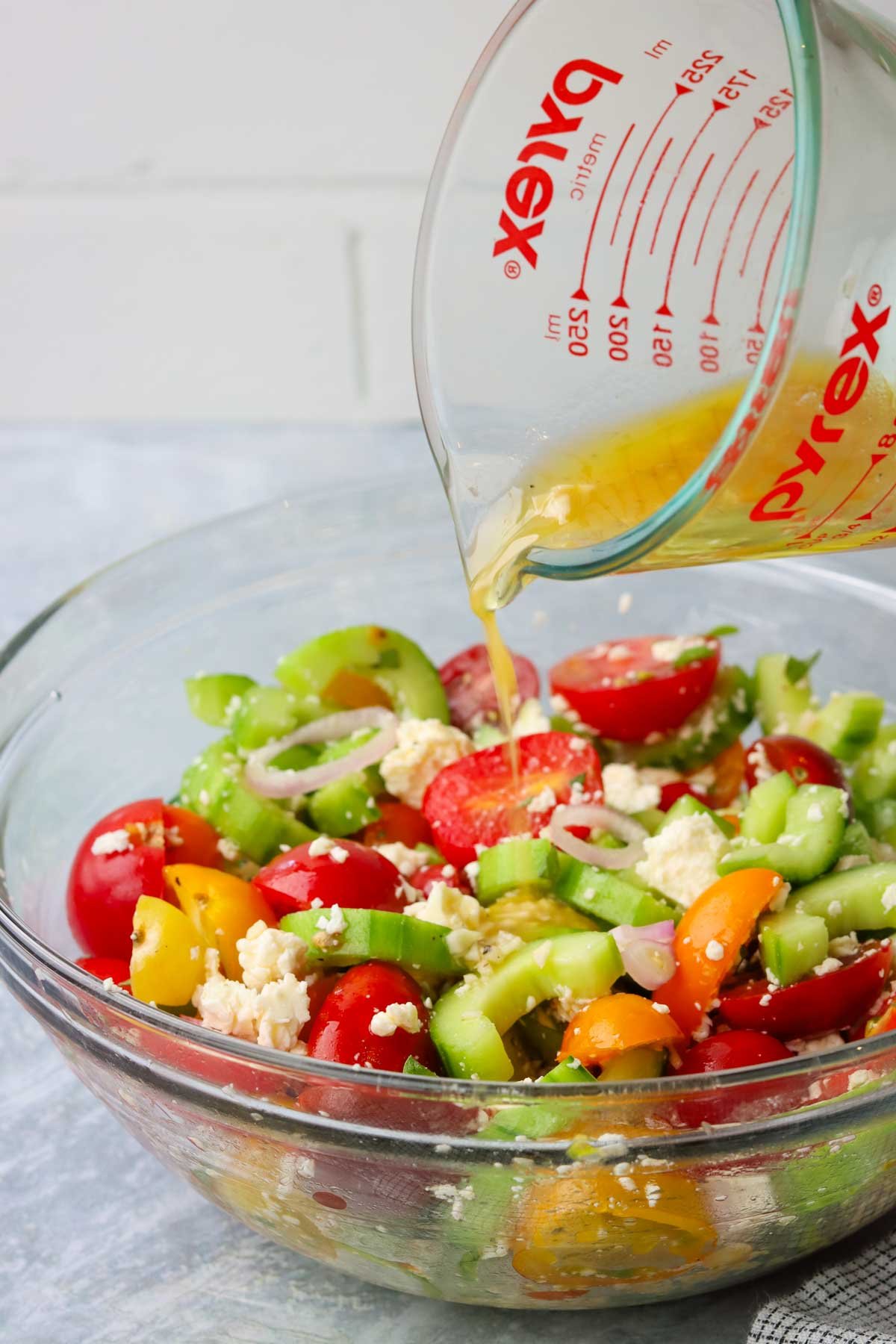 adding dressing to a bowl of tomato cucumber and feta salad