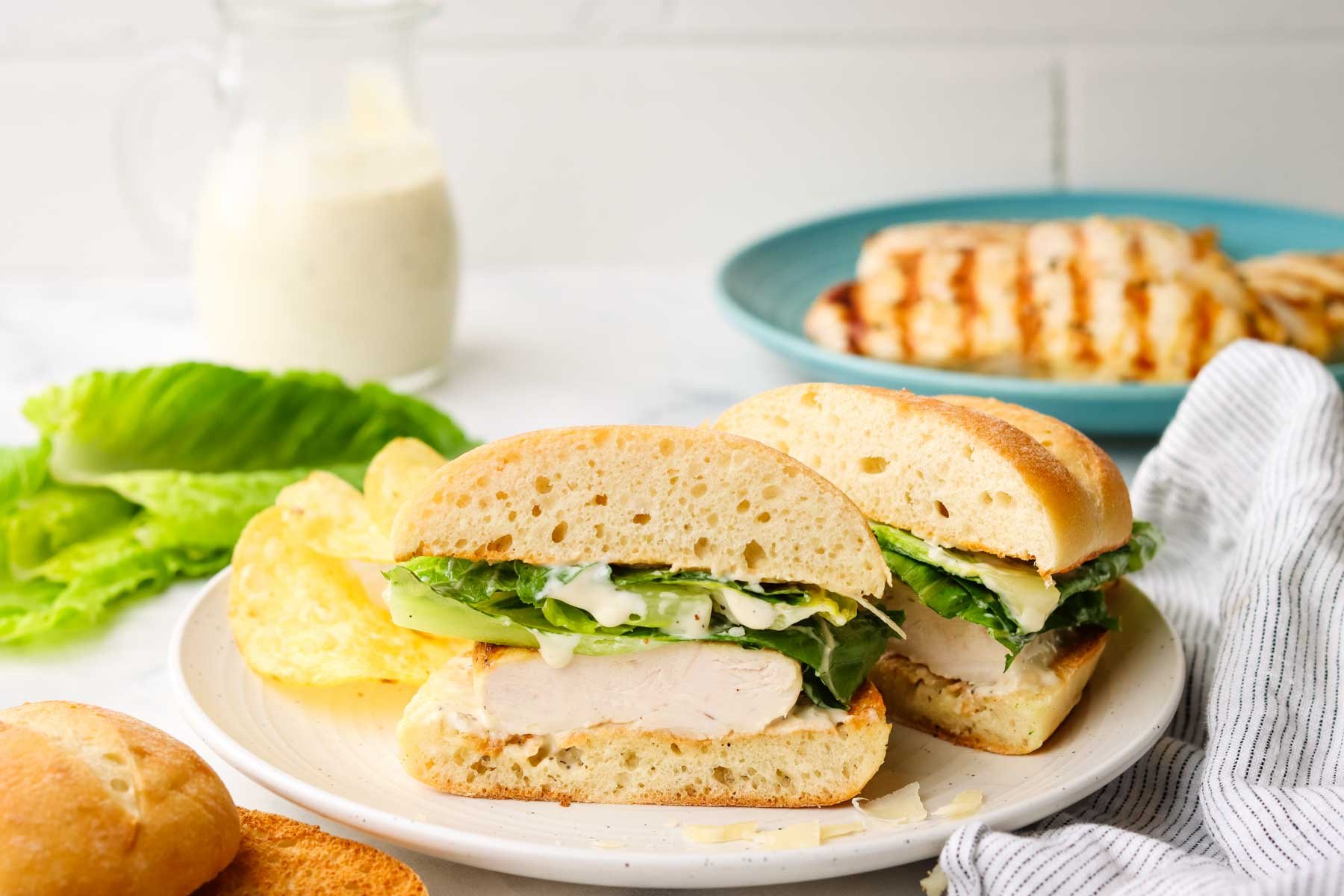 a chicken casar sandwich in a plate cut in half with chips on the side.