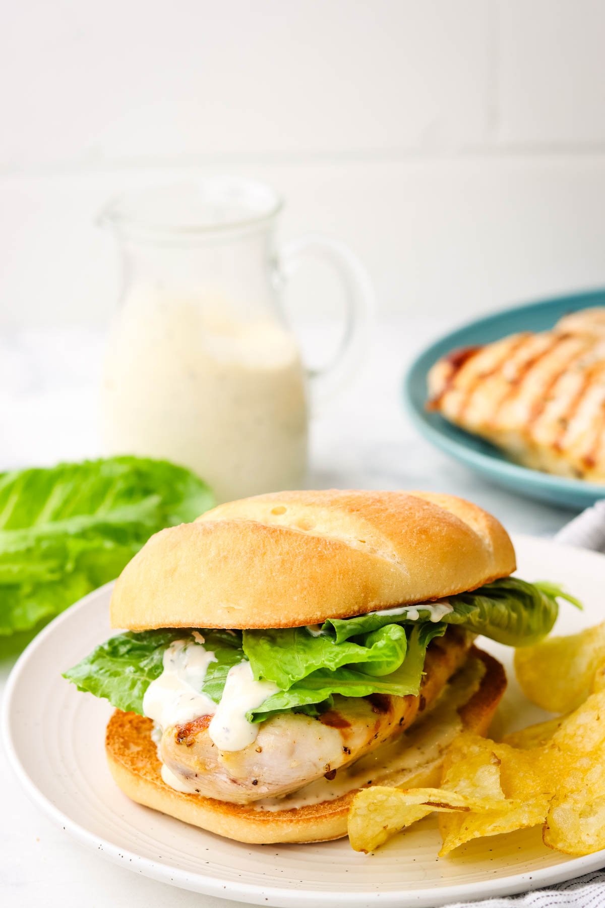 a chicken caesar sandwich served on a plate with a side of chips.