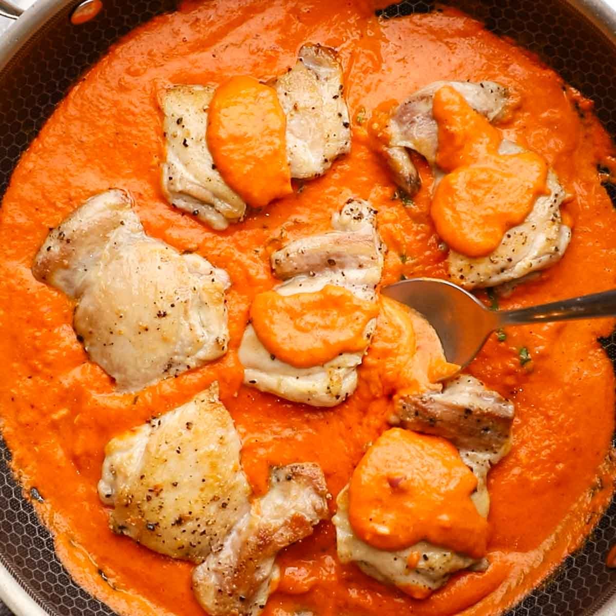spooning sauce over chicken thighs in the skillet
