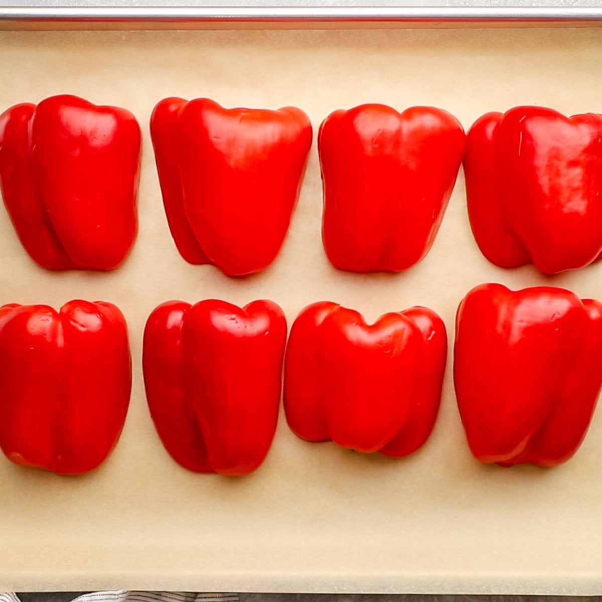 halved red bell peppers cut side down arranged on a baking sheet with parchment paper