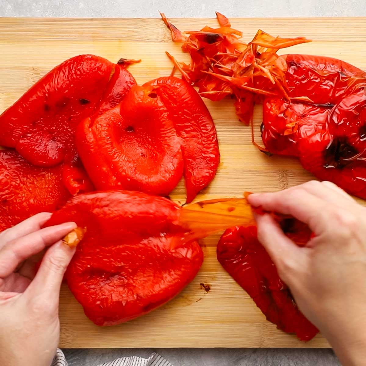 a hand peeling the skin off roasted red bell peppers
