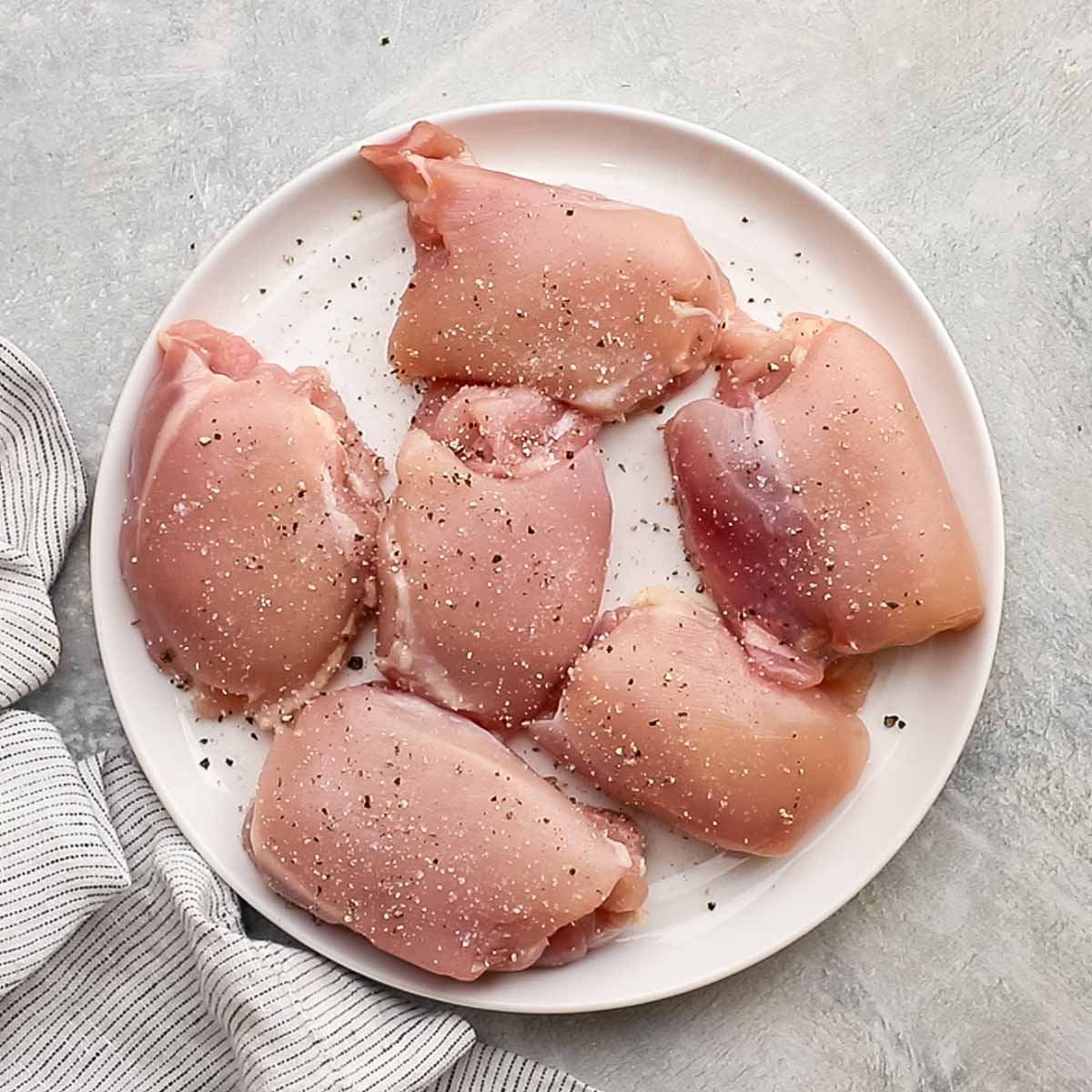 chicken thighs on a plate seasoned with salt and black pepper