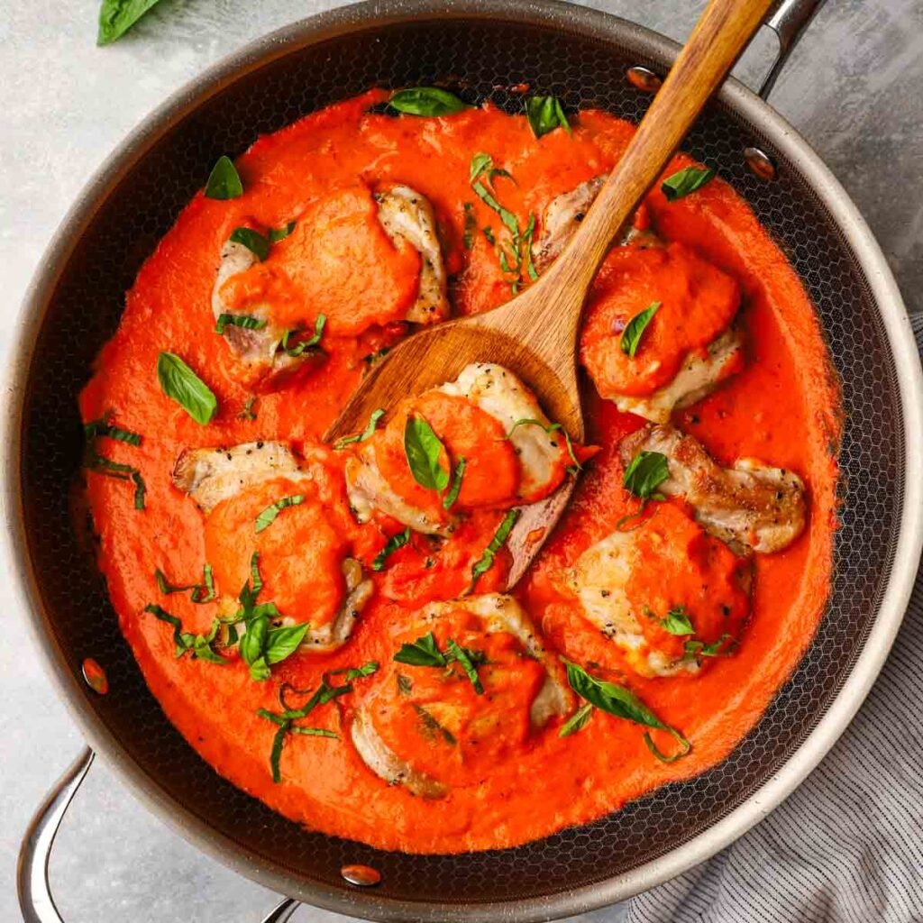 a pan with chicken thighs in a roasted red pepper sauce