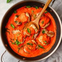 a pan with chicken thighs in a roasted red pepper sauce