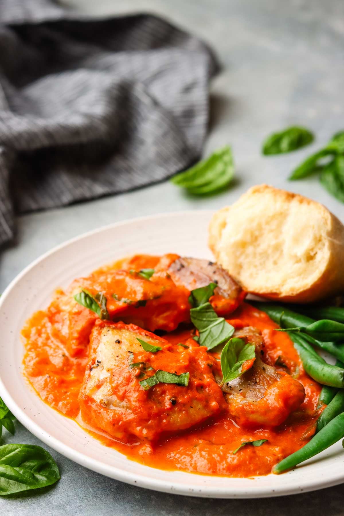 a plate served with roasted red pepper chicken and green beans with a side of bread