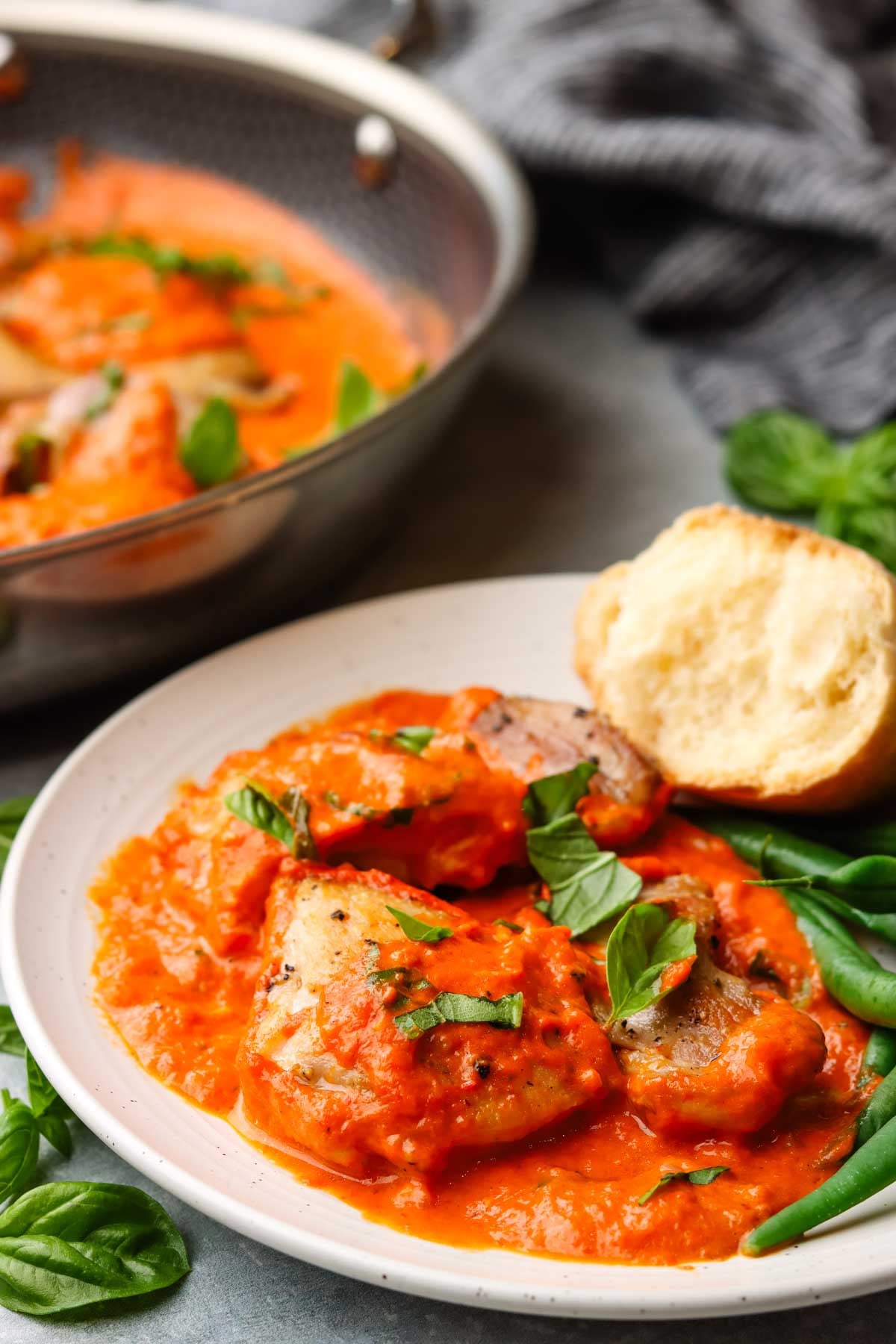 a plate served with roasted red pepper chicken and green beans with a side of bread