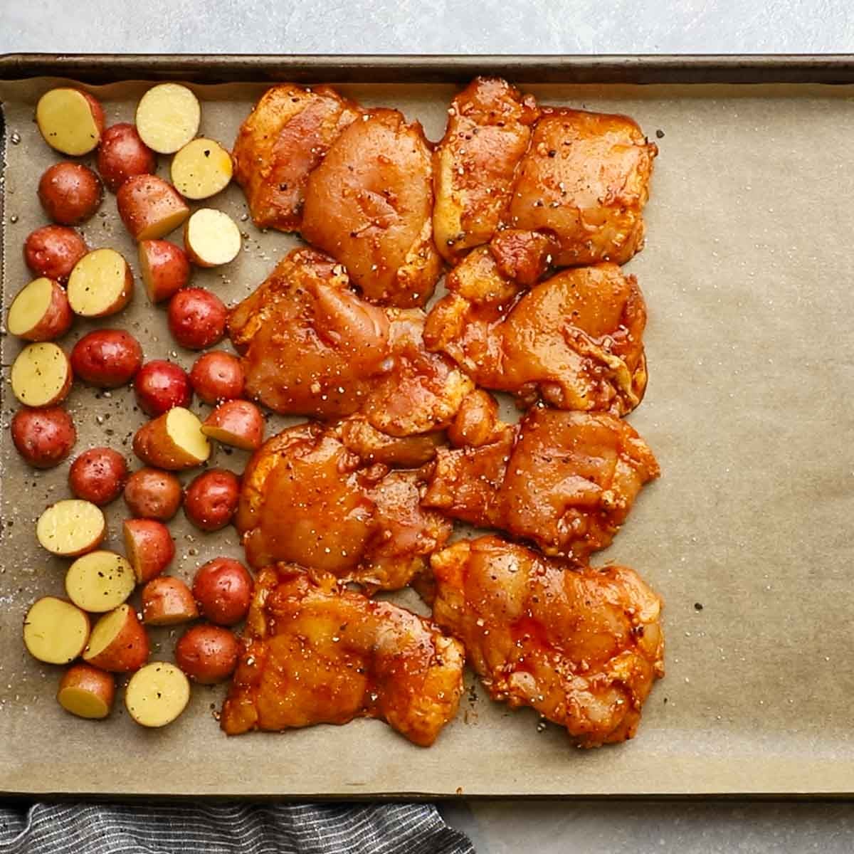 marinated chicken thighs and potatoes spread on a baking sheet