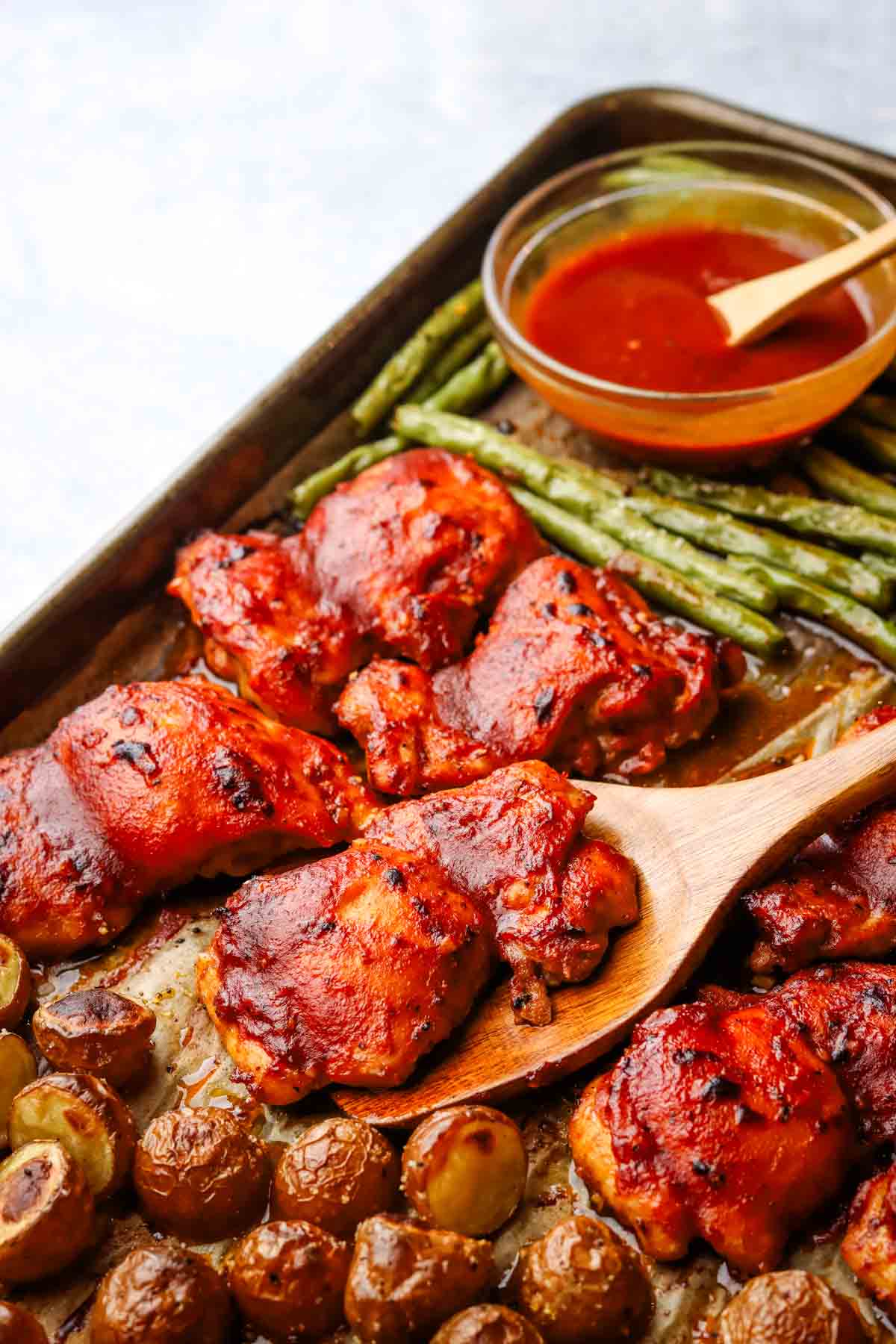 a baking dish with chicken thighs, green beans, and roasted potatoes with some sauce in a bowl.