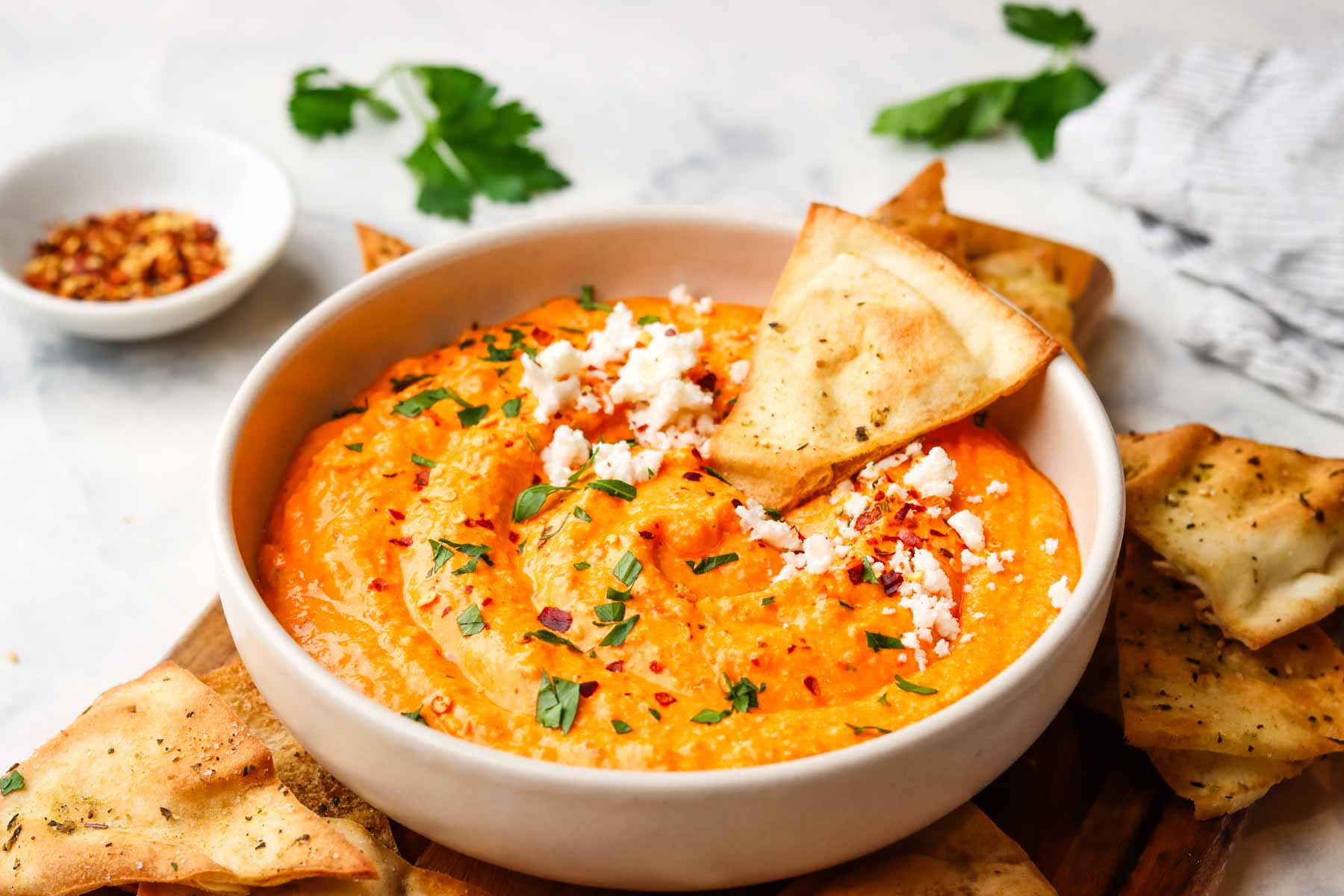 a bowl of feta and roasted red pepper dip with a crunchy pita on the side