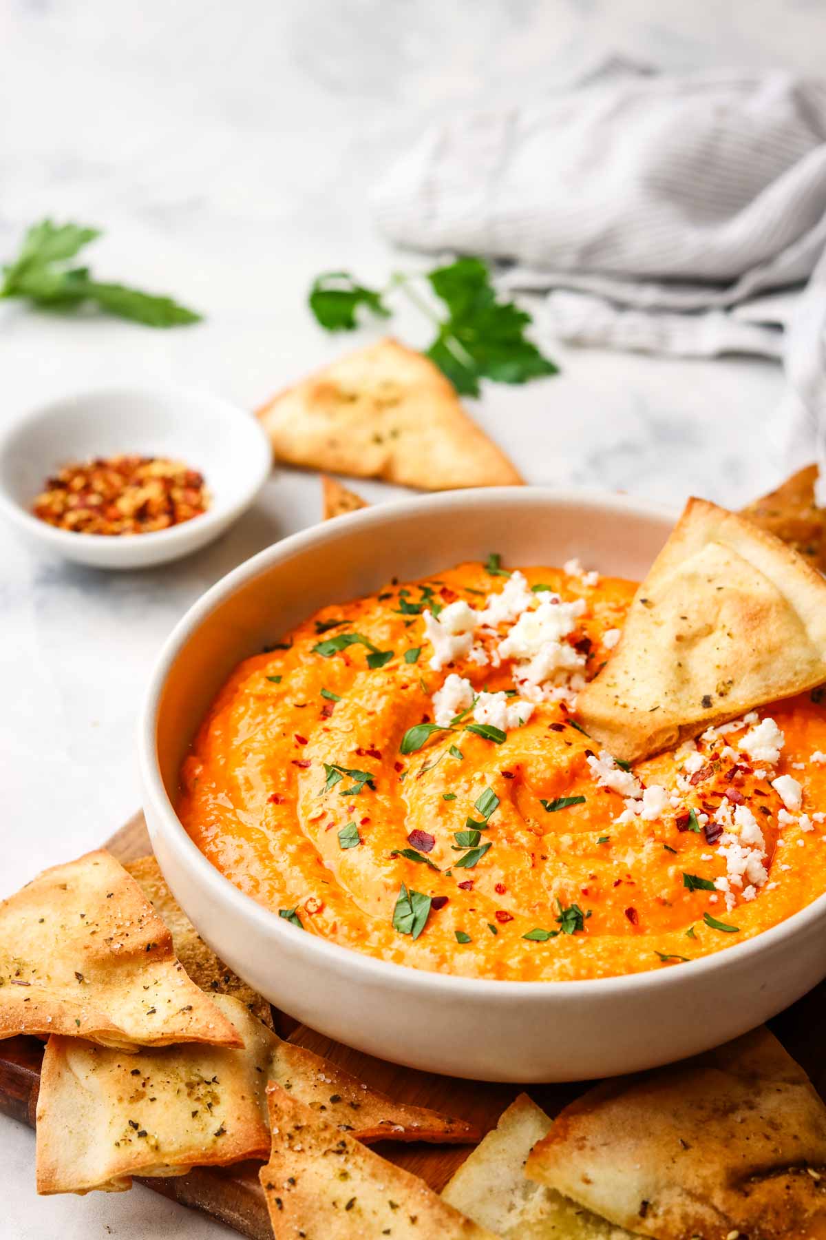 a pita chip dipped in a bowl of feta and roasted red pepper dip