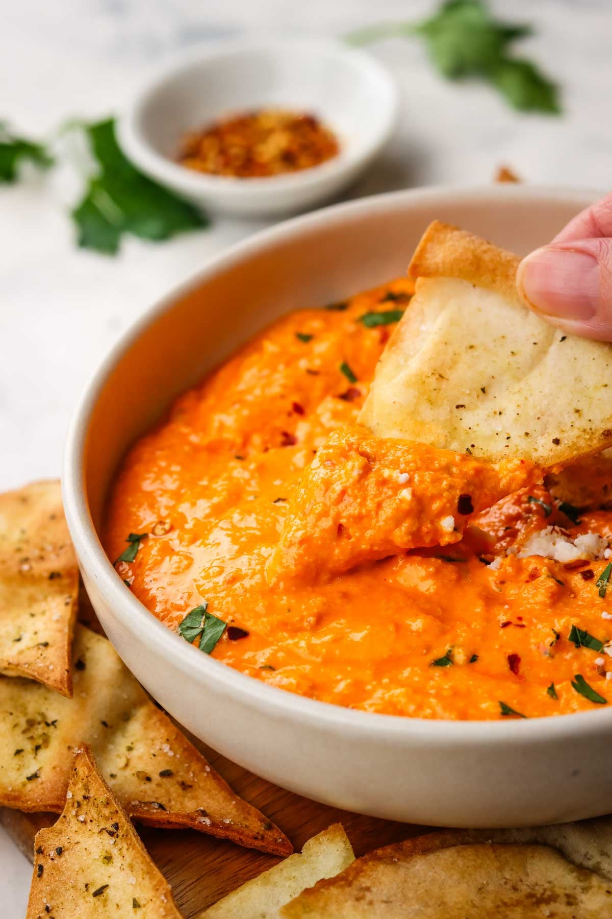 a bowl of feta and roasted red pepper dip with crunchy pita dipped in the bowl and more on the side