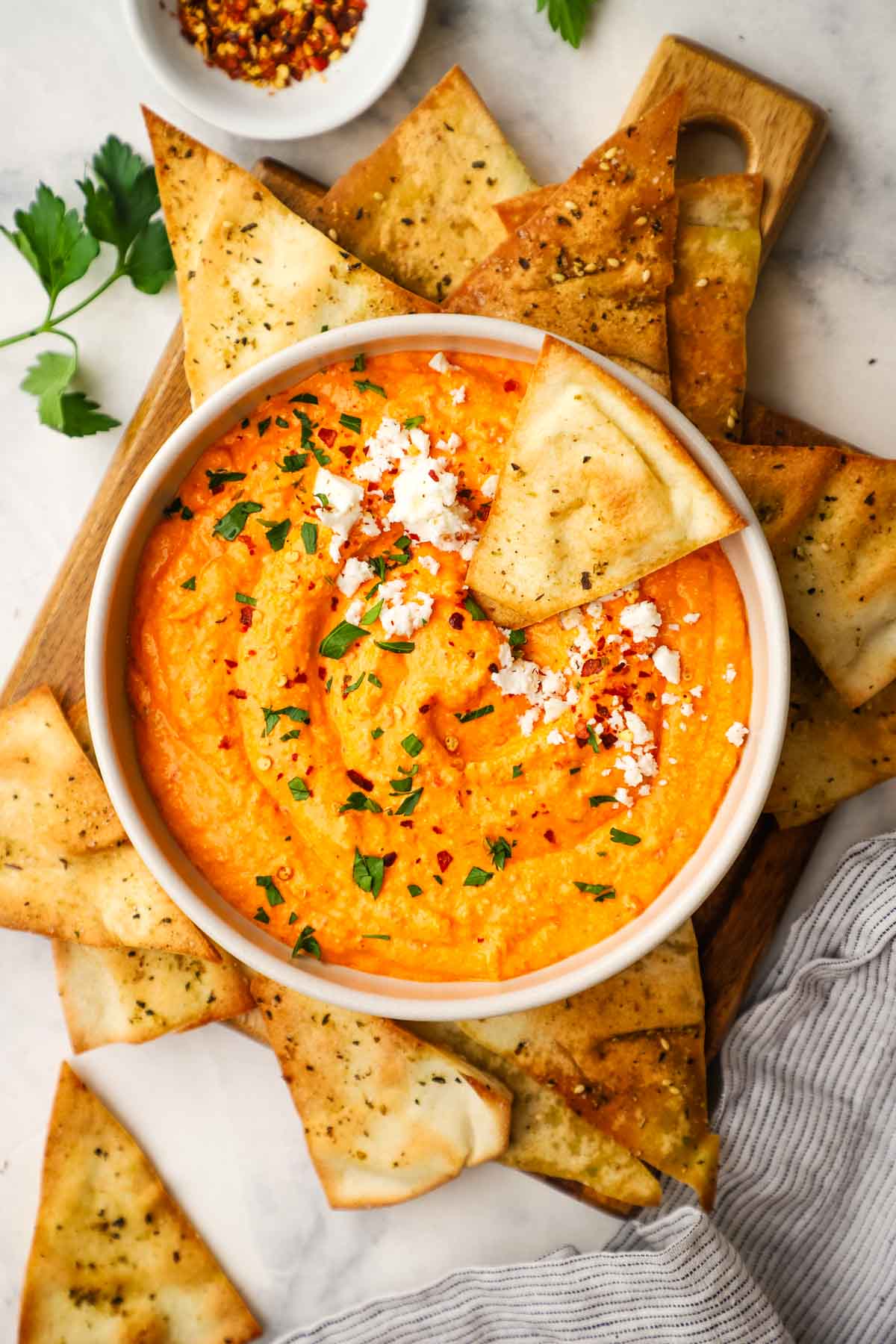 a bowl of feta and roasted red pepper dip in a bowl with a pita chip dipped in the bowl and more crunchy pitas on the side