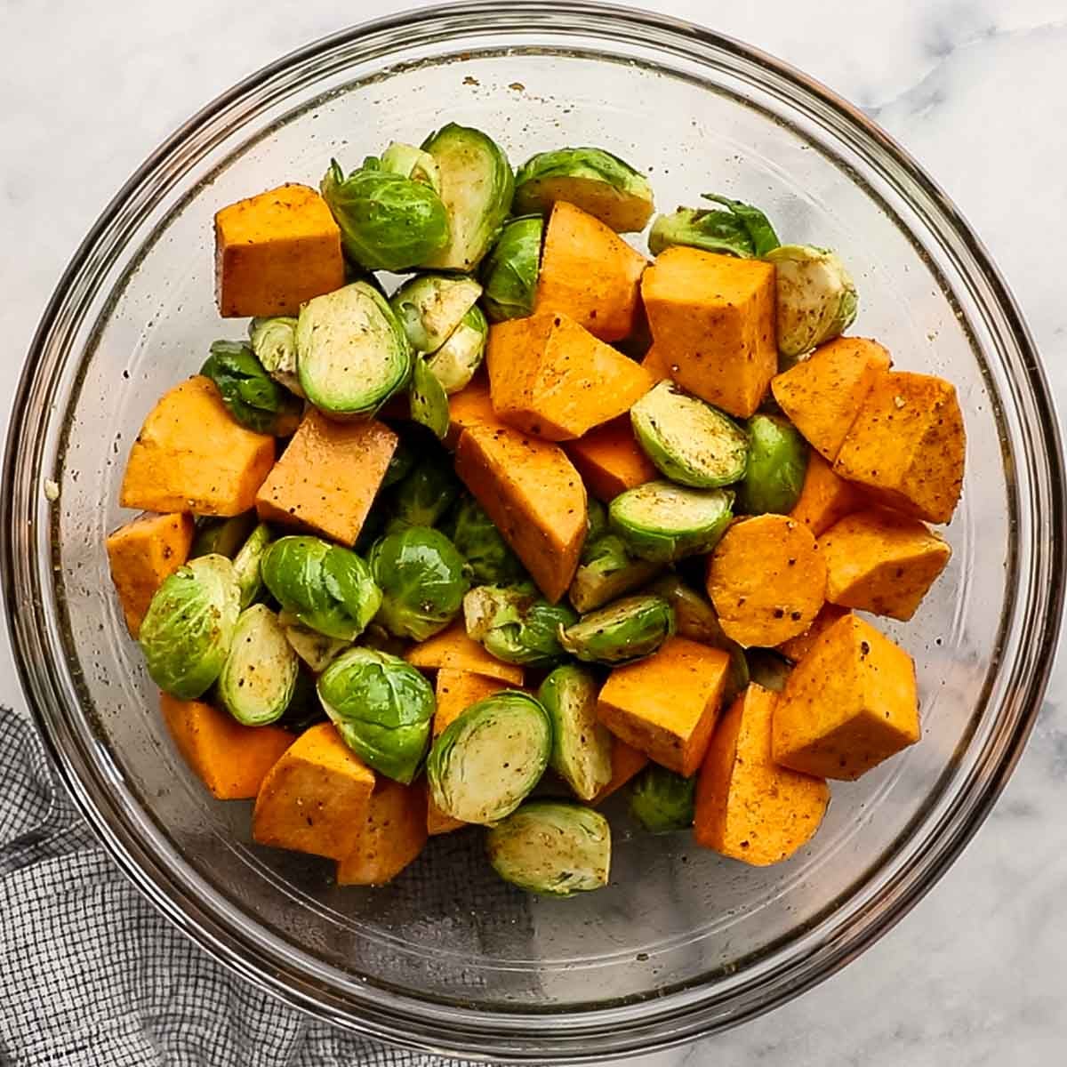 spices and seasonings added to the bowl of cut up sweet potatoes and Brussels sprouts