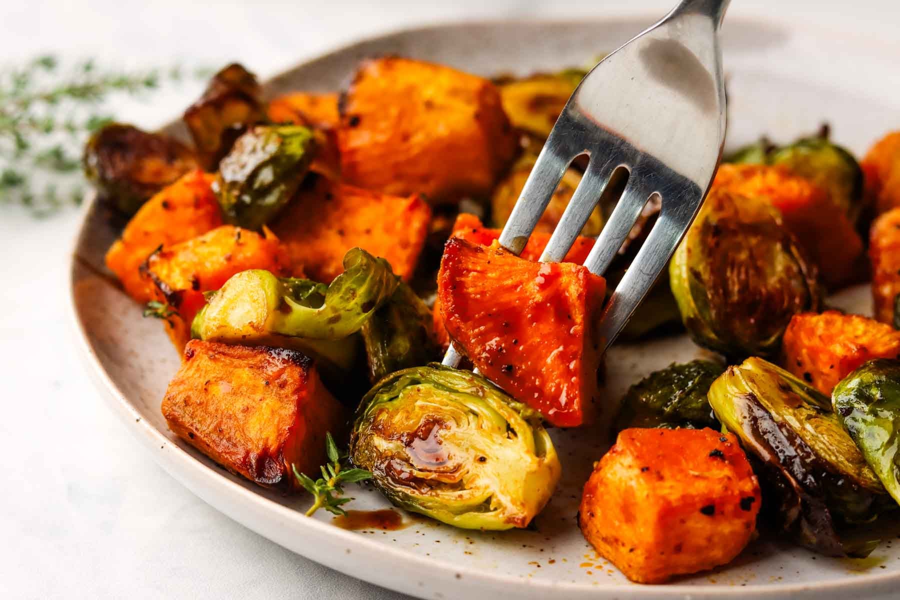 a fork picking up a piece of roasted vegetables from a plate of roasted brussels sprouts and sweet potatoes