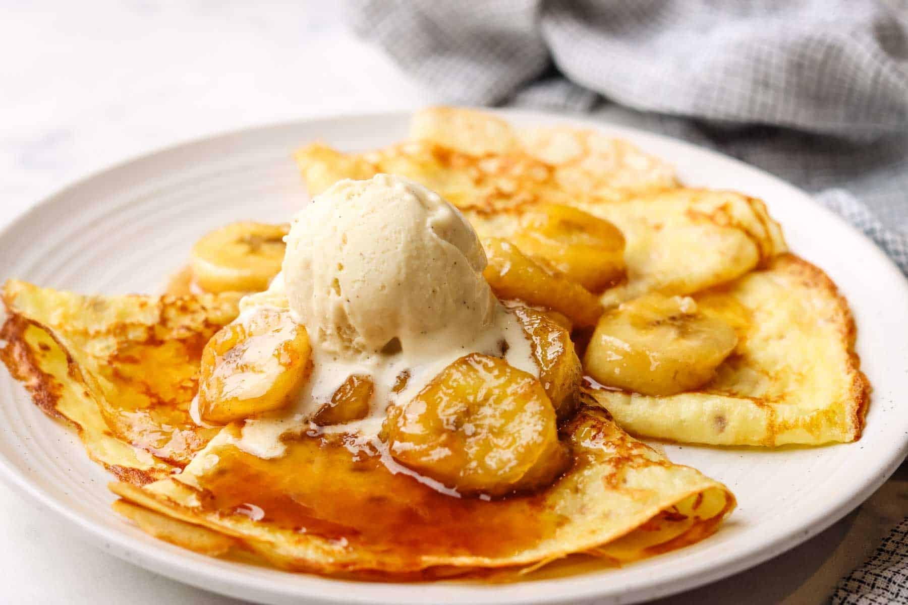 a plate of crepes with banana foster topping and a scoop of vanilla icecream