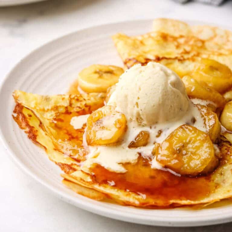 a plate of crepes with banana foster topping and a scoop of vanilla icecream