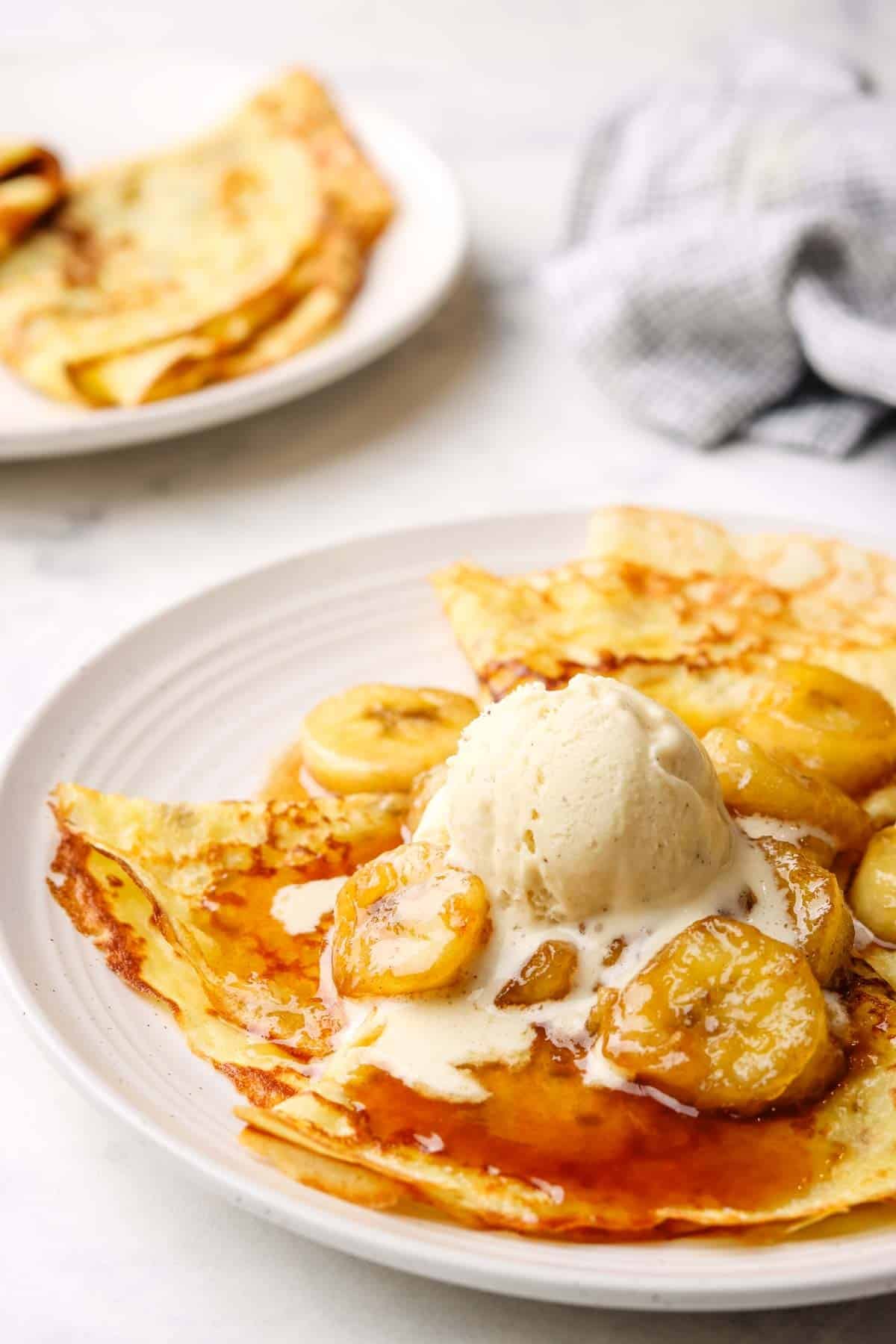 a plate of crepes with banana foster topping and a scoop of vanilla icecream