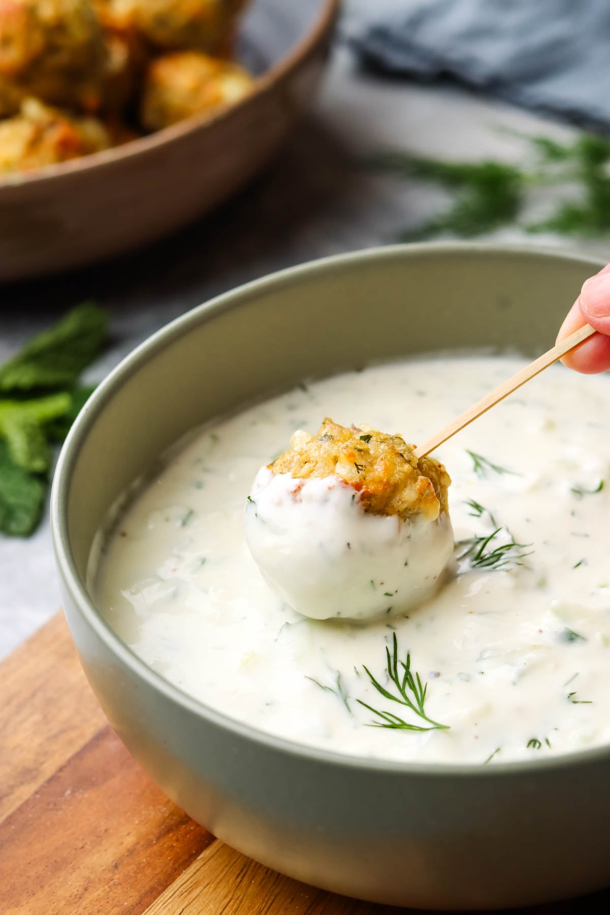 a hand dipping a meatball in a bowl of cucumber yogurt dip