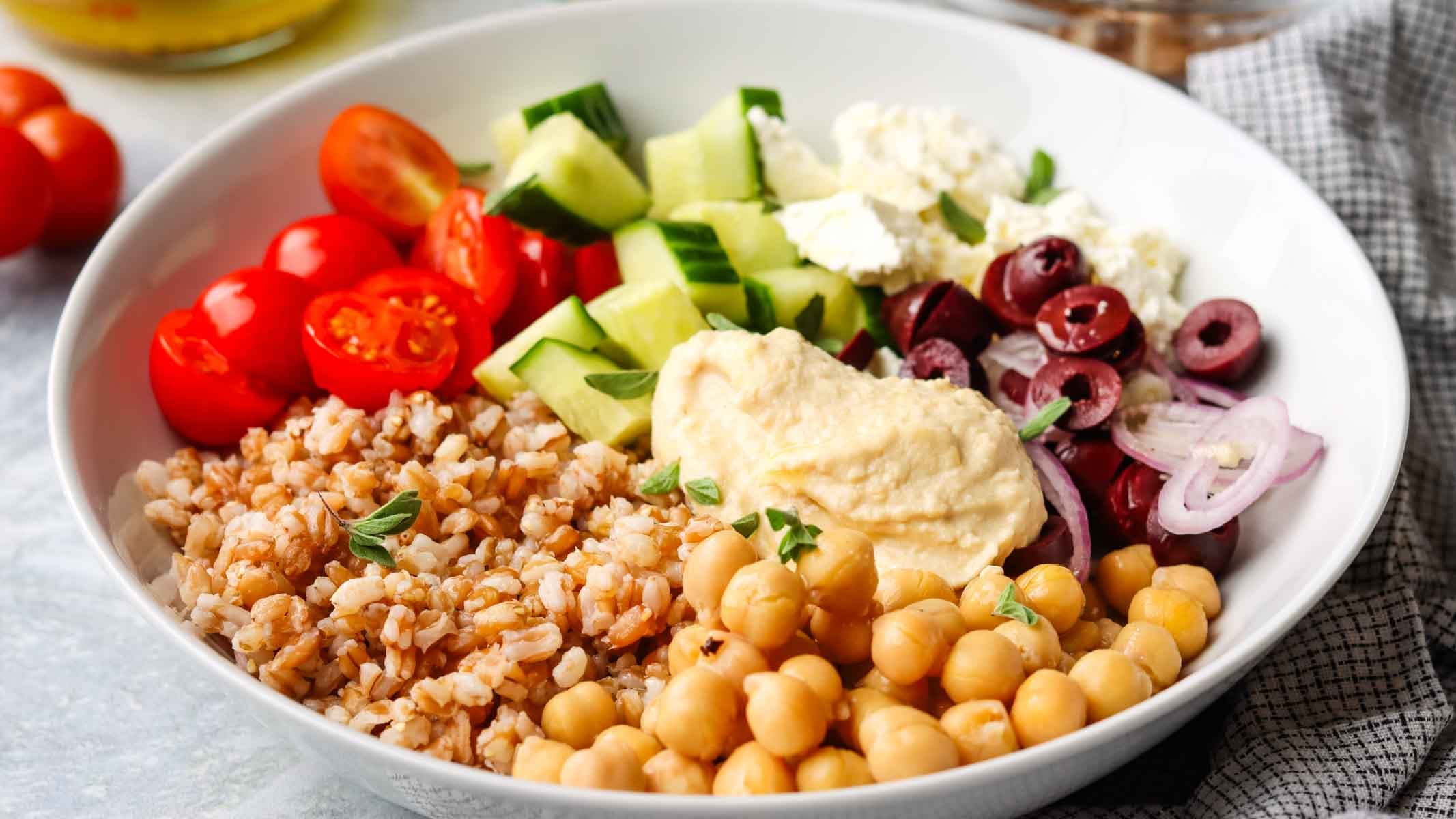 a loaded bowl with fresh veggies, farro, chickpeas and hummus.
