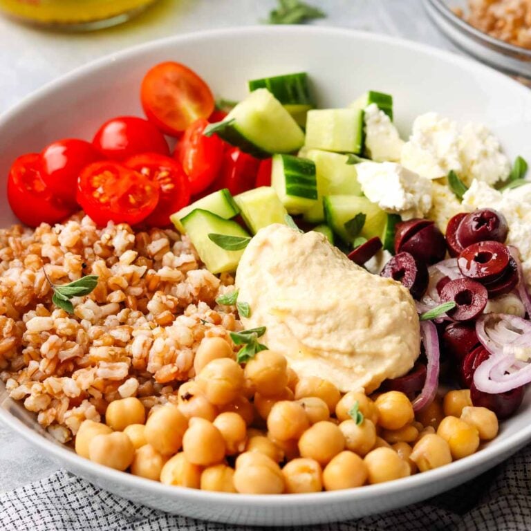 a loaded bowl with fresh veggies, farro, chickpeas and hummus.