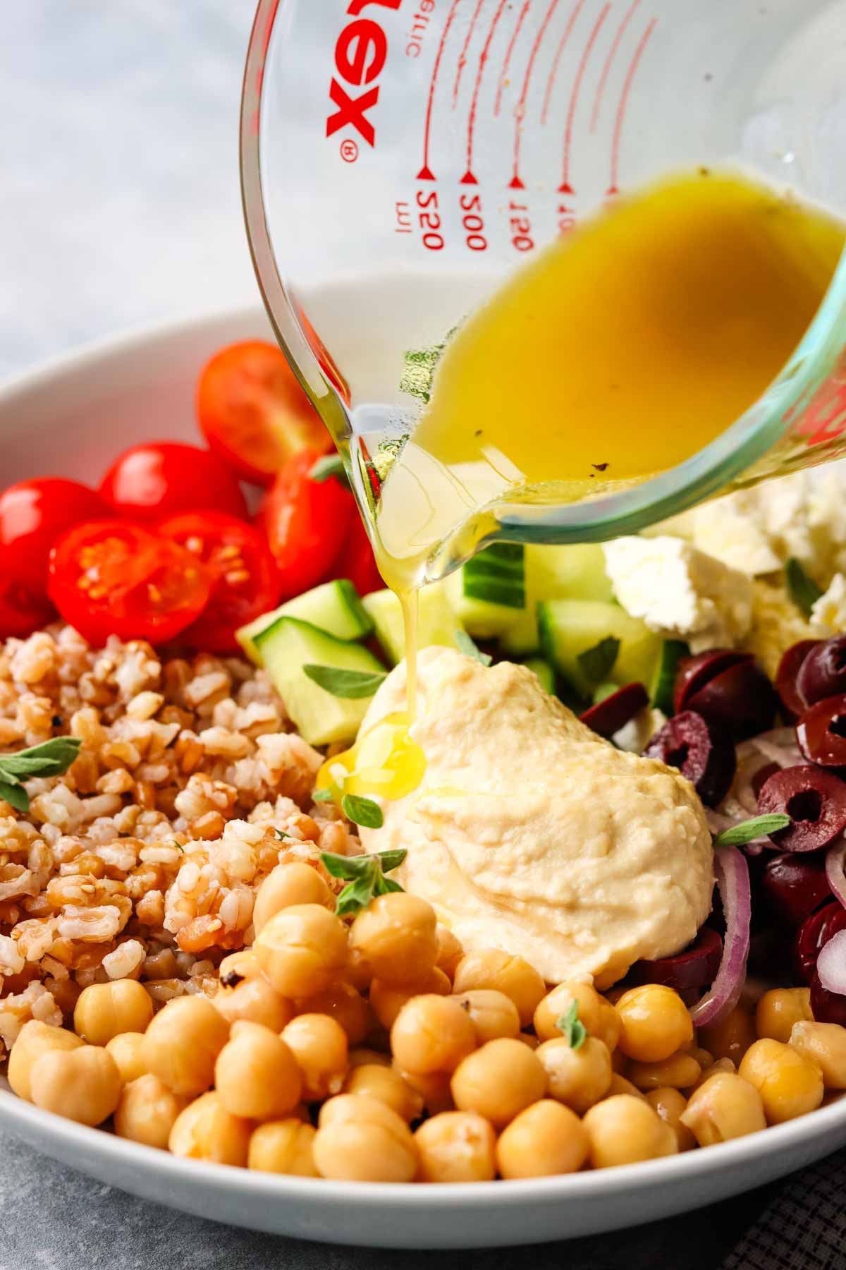 pouring dressing over a farro bowl
