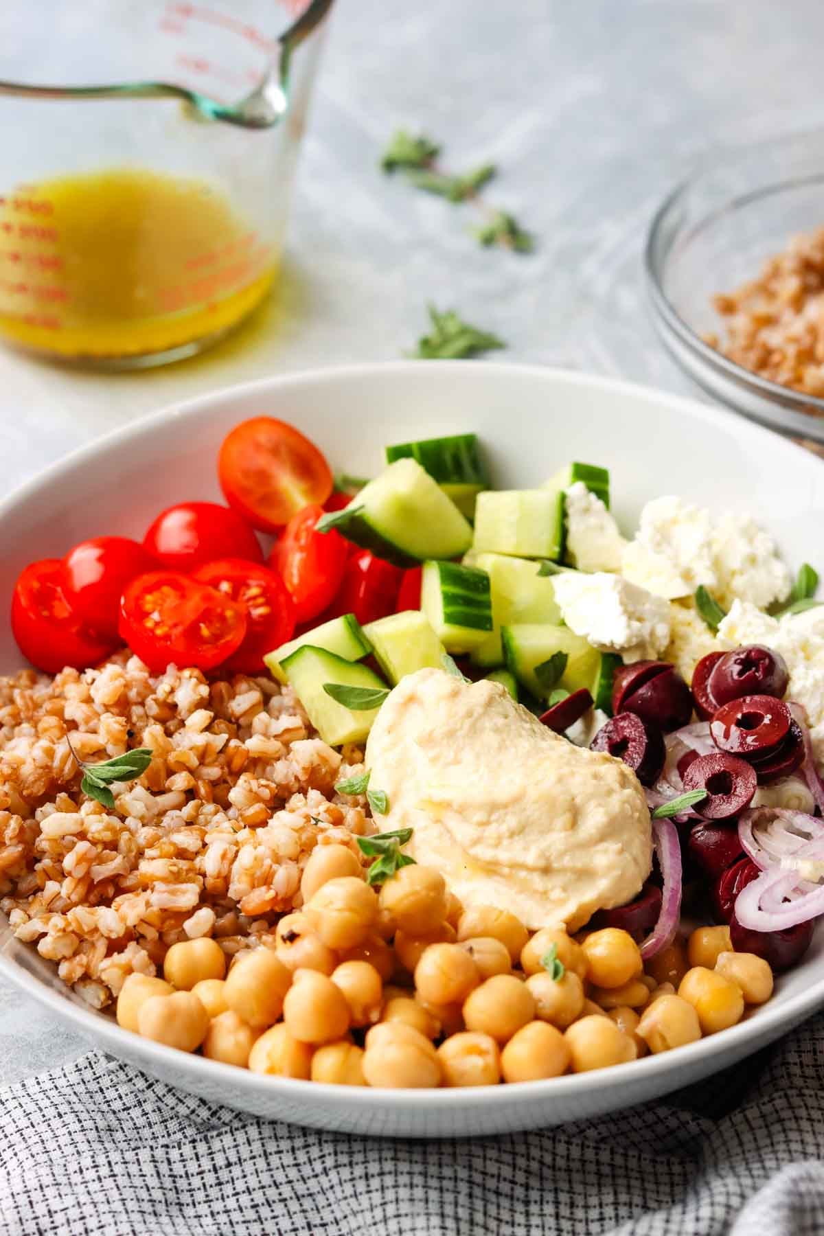 a loaded bowl with fresh veggies, farro, chickpeas and hummus.