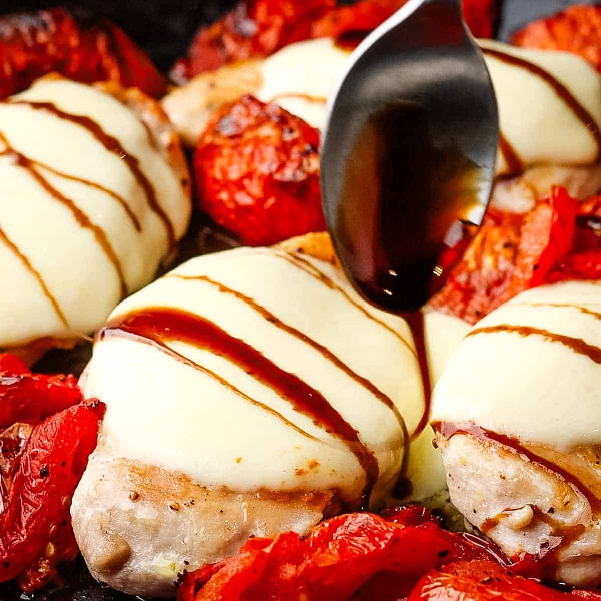 Balsamic glaze being drizzled over mozzarella topped chicken breasts.