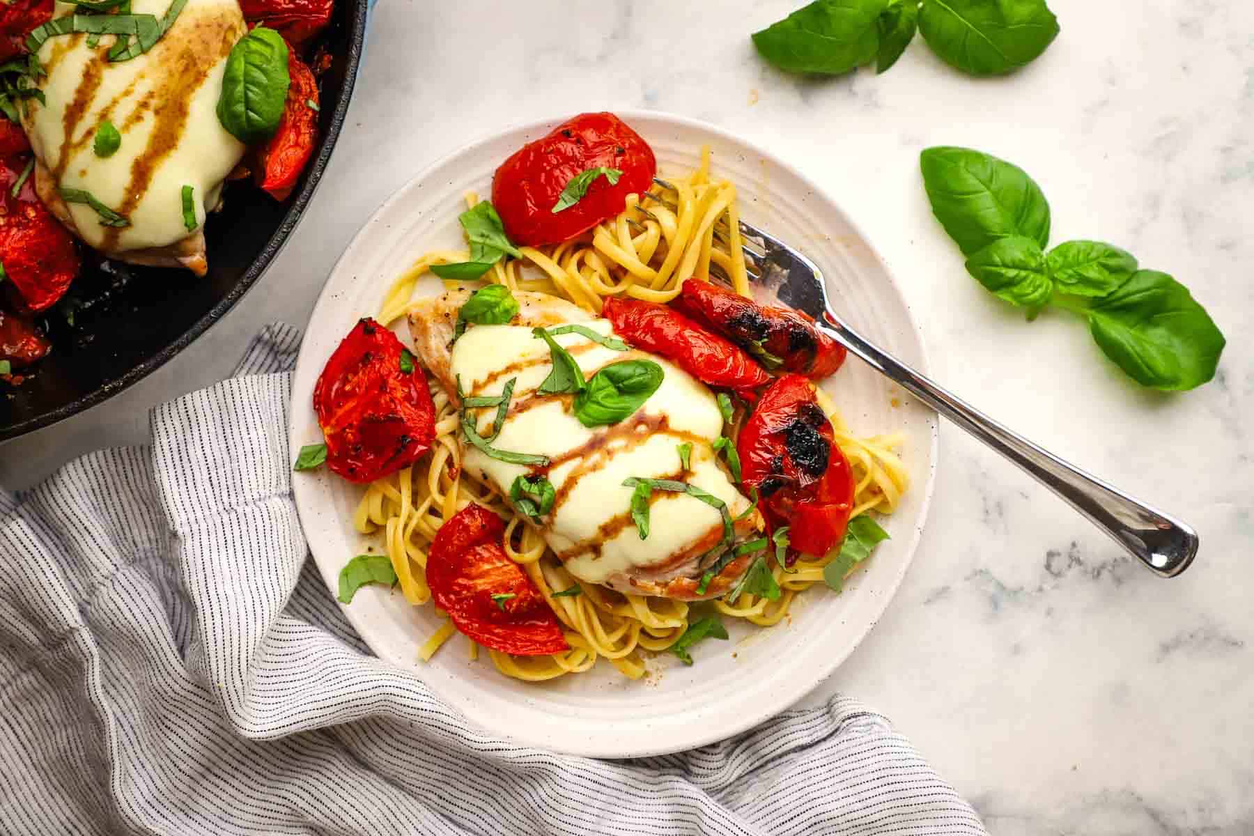 A plate of caprese chicken over linguine with roasted tomatoes.