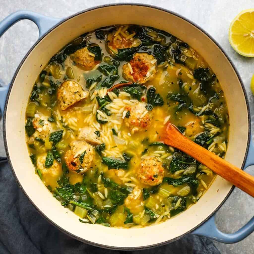 A pot of chicken meatball soup with spinach and orzo.