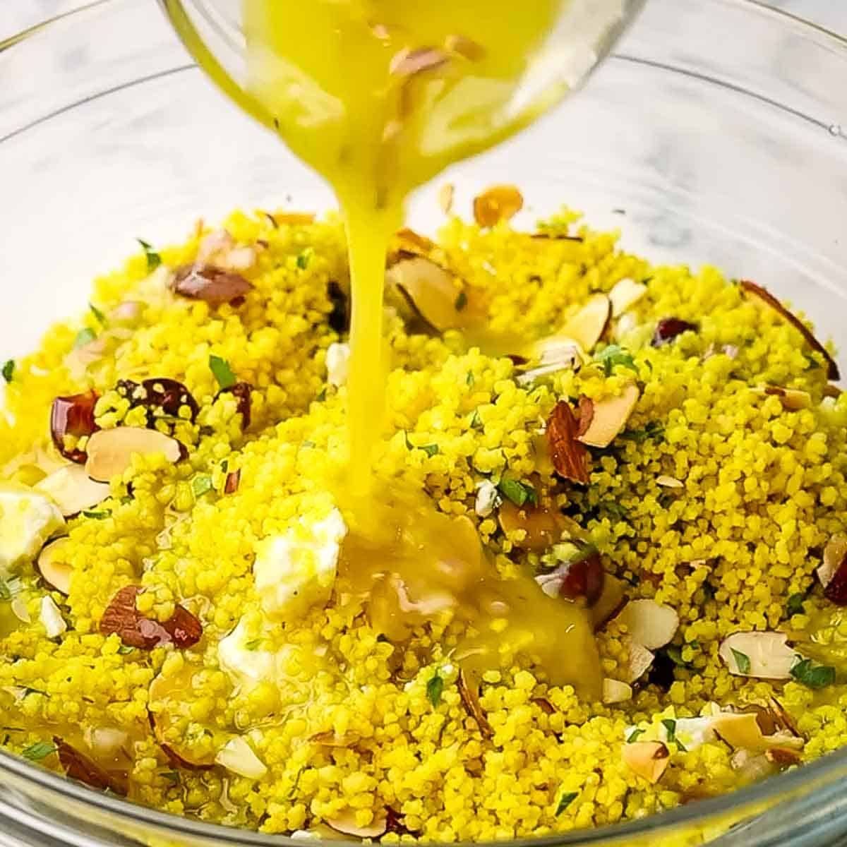 Dressing being poured over a couscous salad.