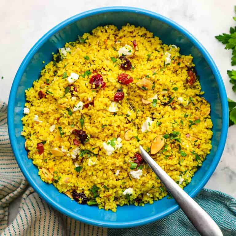 A serving bowl of curried couscous salad with a serving spoon in it.
