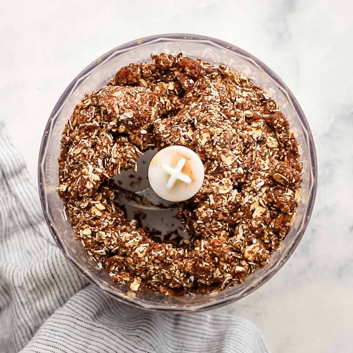 Blended ingredients for chocolate peanut butter protein balls inside a food processor ready to be rolled into small balls.