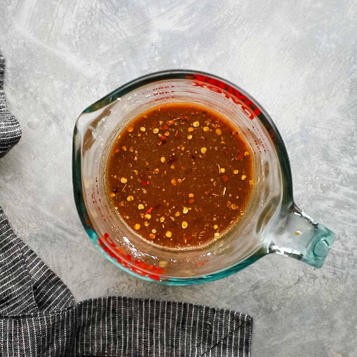 Top-down view of a glass bowl that contains mixed ingredients of chicken stock, hoisin sauce, soy sauce, rice vinegar, sesame oil, sugar, and red pepper flakes for stir-fry sauce.