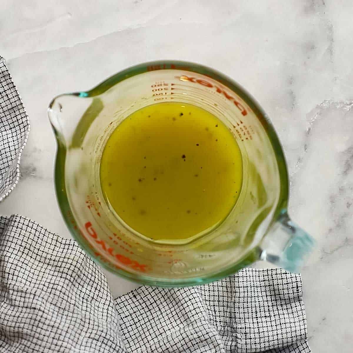A glass bowl mix of olive oil, white balsamic vinegar, lemon juice, and salt is mixed for the vinaigrette dressing.