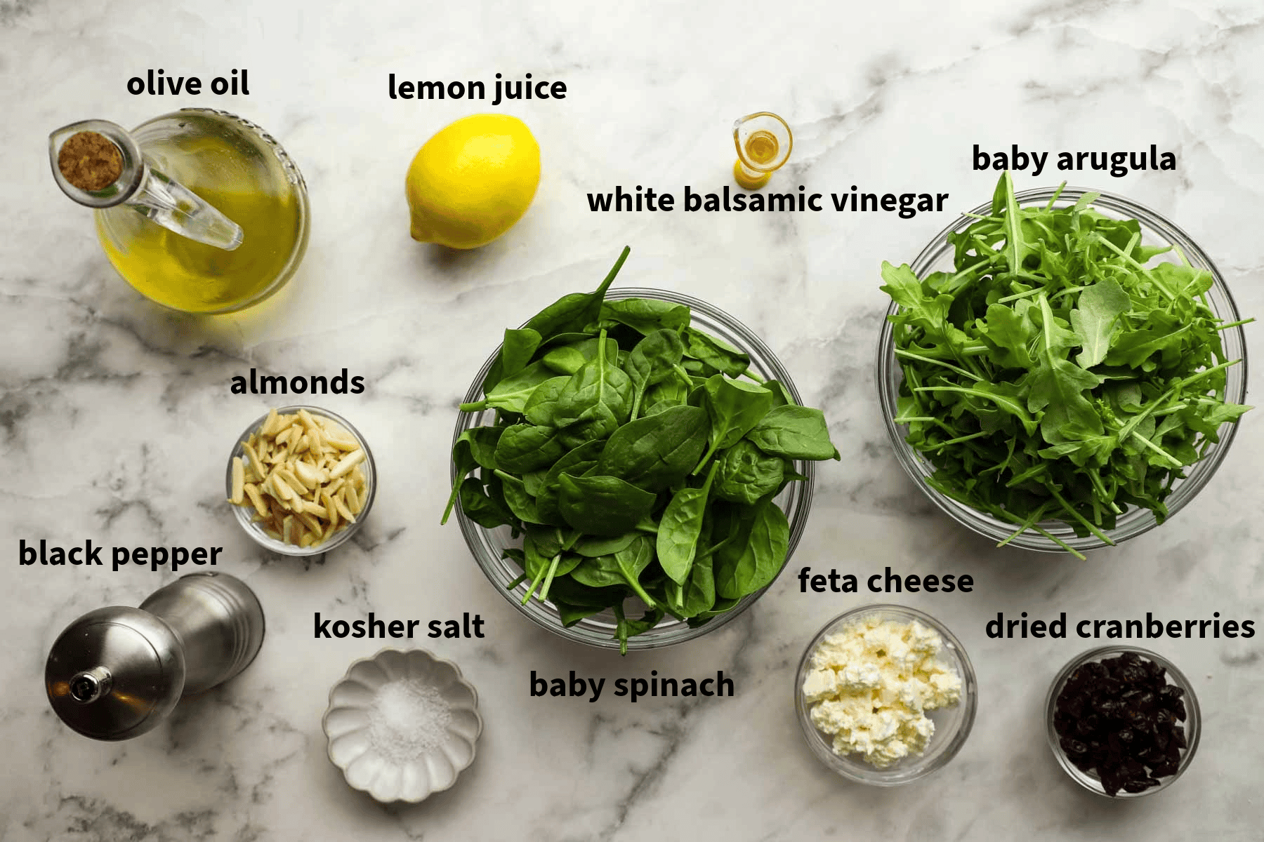 Top-down view of spinach salad recipe that include lemon juice, white balsamic vinegar, feta cheese, salad, sliced almonds, and more.