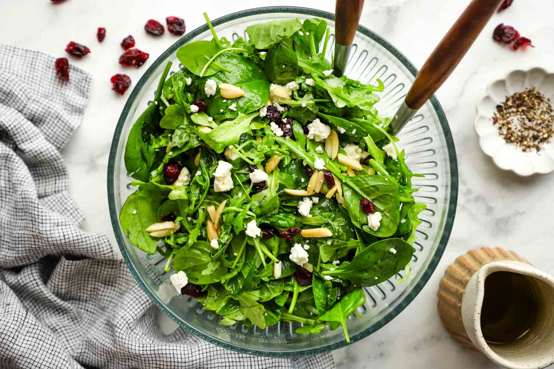 Spinach arugula salad top-down view with feta, cranberries, and almond slices, in a glass serving bowl.