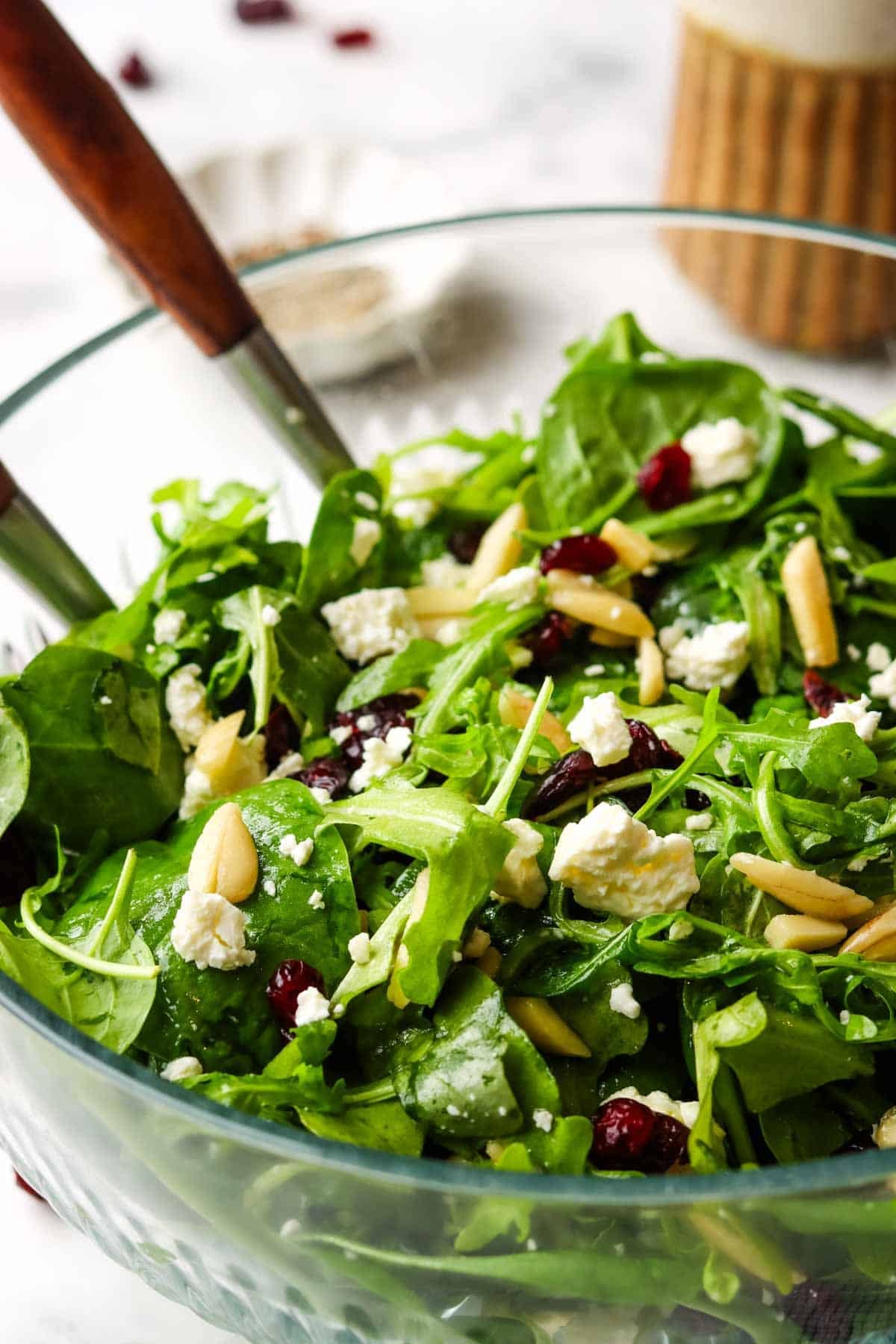 A bowl of greens topped with almonds, cranberries, and feta cheese.